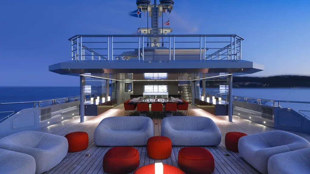 The aft bridge deck at dusk, with lounge chairs, red stools and a dining table under the overhang