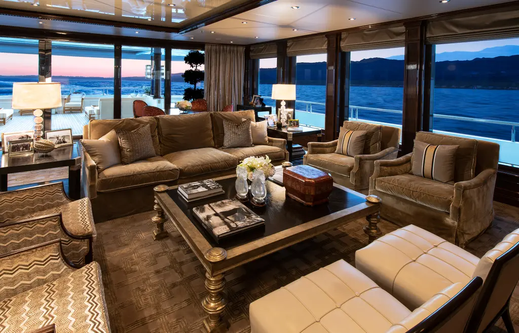 Main saloon with velvet sofas, a large coffee table and windows along both sides