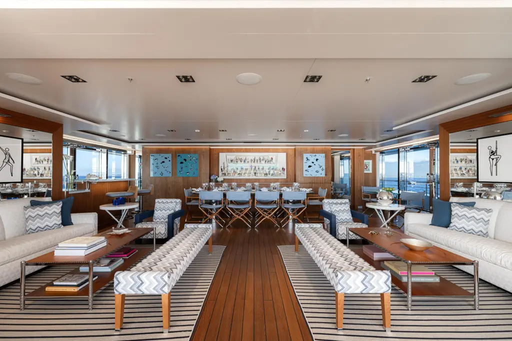 Long main saloon with sofas, benches and a dining table set for many guests, with windows on both sides