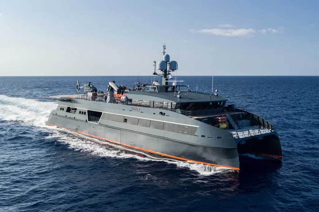 Hodor at sea seen from ahead and above, showing her angular grey superstructure, a mast with radar domes and the twin hulls with orange trim at the waterline