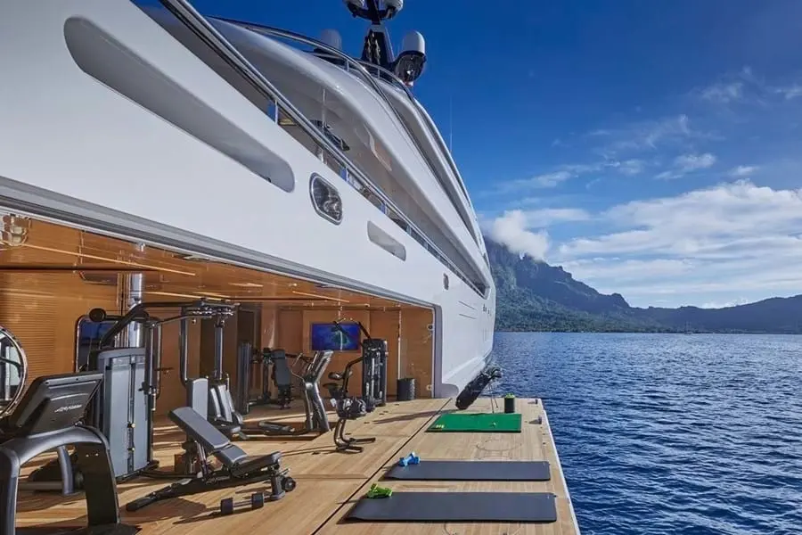Gym with exercise machines opening onto a fold-down terrace just above the sea, green mountains in the distance