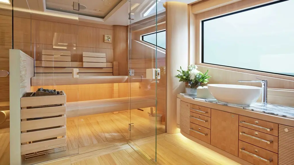 Spa with a glass-fronted sauna in pale wood next to a washbasin and a large window