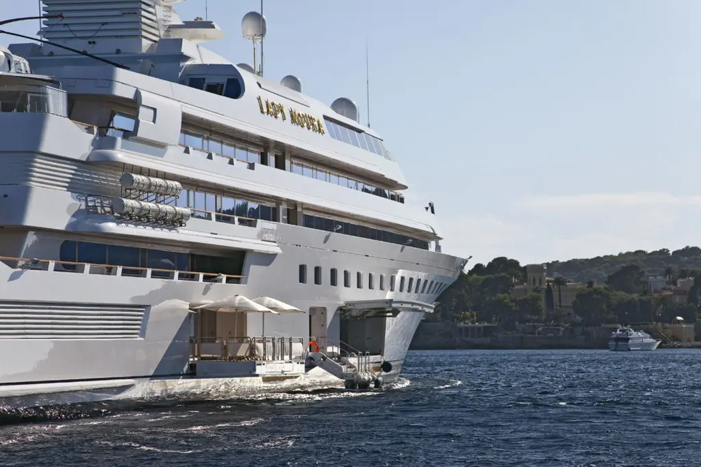 Side of Lady Moura with her name in gold letters and a terrace with parasols at water level