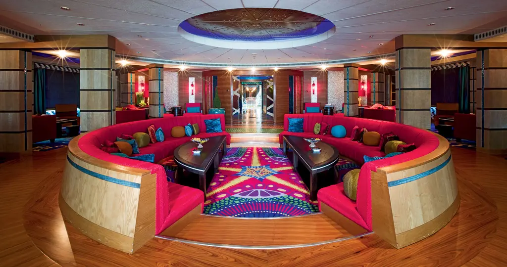 Sunken circular lounge with red sofas around two dark tables and a patterned carpet under a domed ceiling