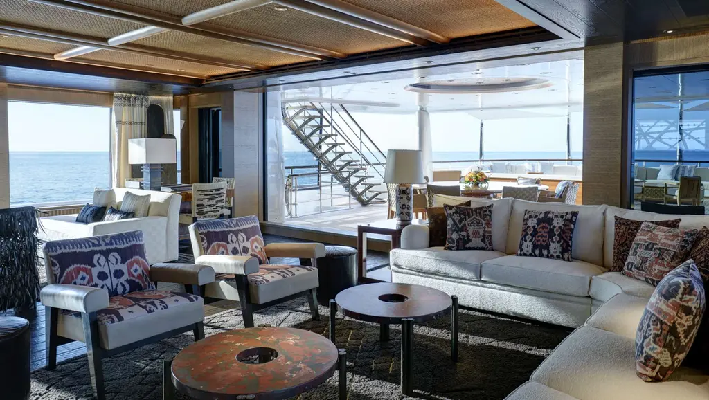 Saloon with sofas and patterned armchairs, glass doors open onto the aft deck and a staircase