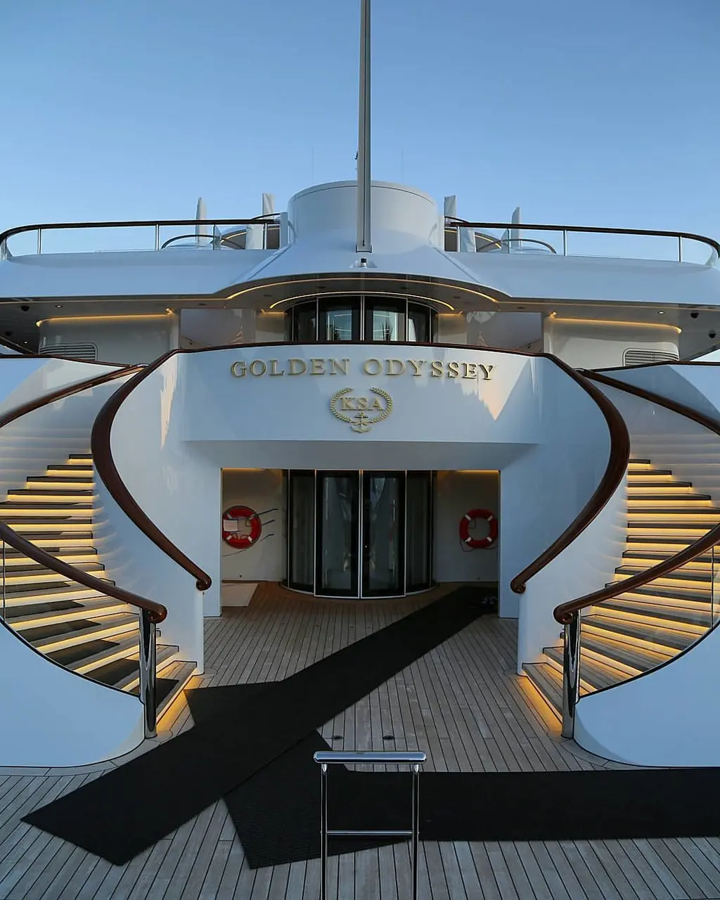 Two curved staircases with teak handrails and lit steps leading down to Golden Odyssey's stern deck