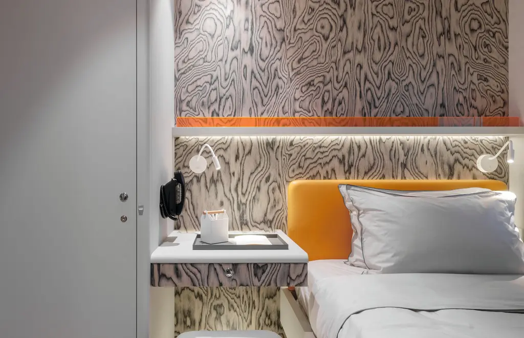 A crew cabin with an orange leather headboard, a white bed, and a black and white swirled veneer on the wall behind