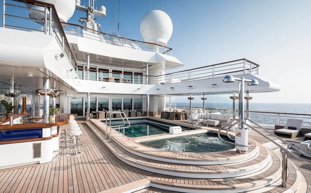 Teak bridge deck with a bar, the long swimming pool and a round spa pool, open sea beyond the rail