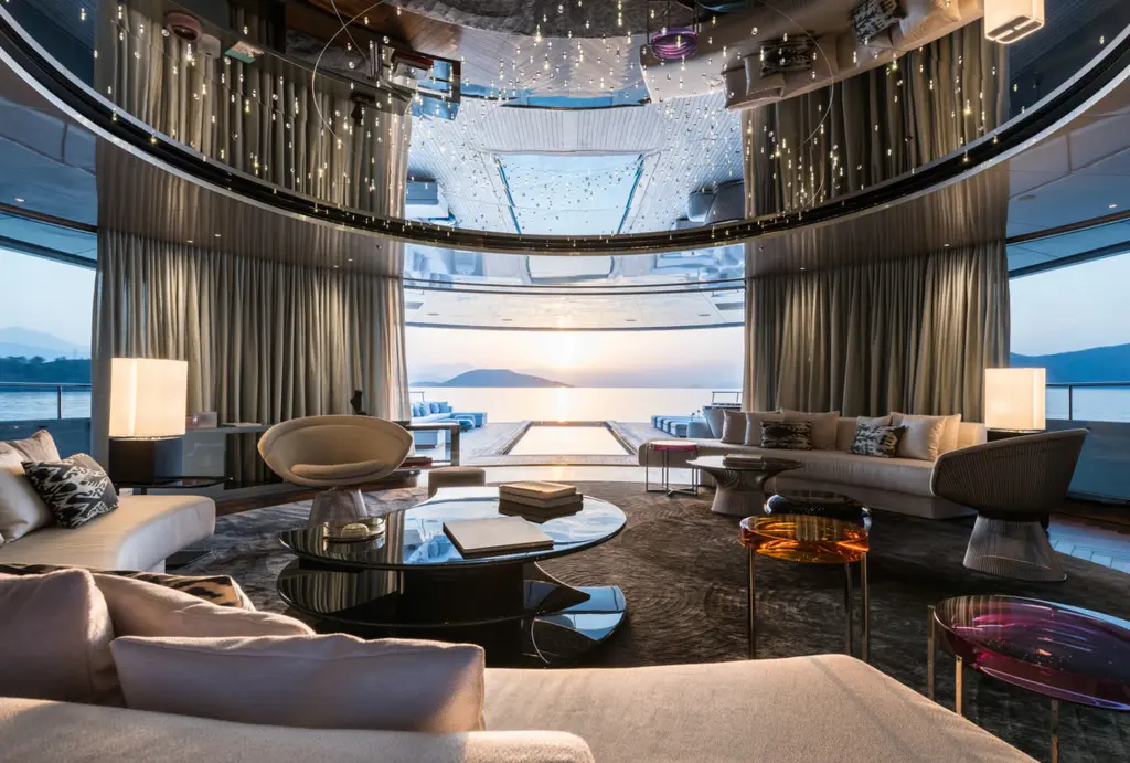 The main saloon with grey sofas, a round glass table and a mirrored, light-studded ceiling, with sea views aft