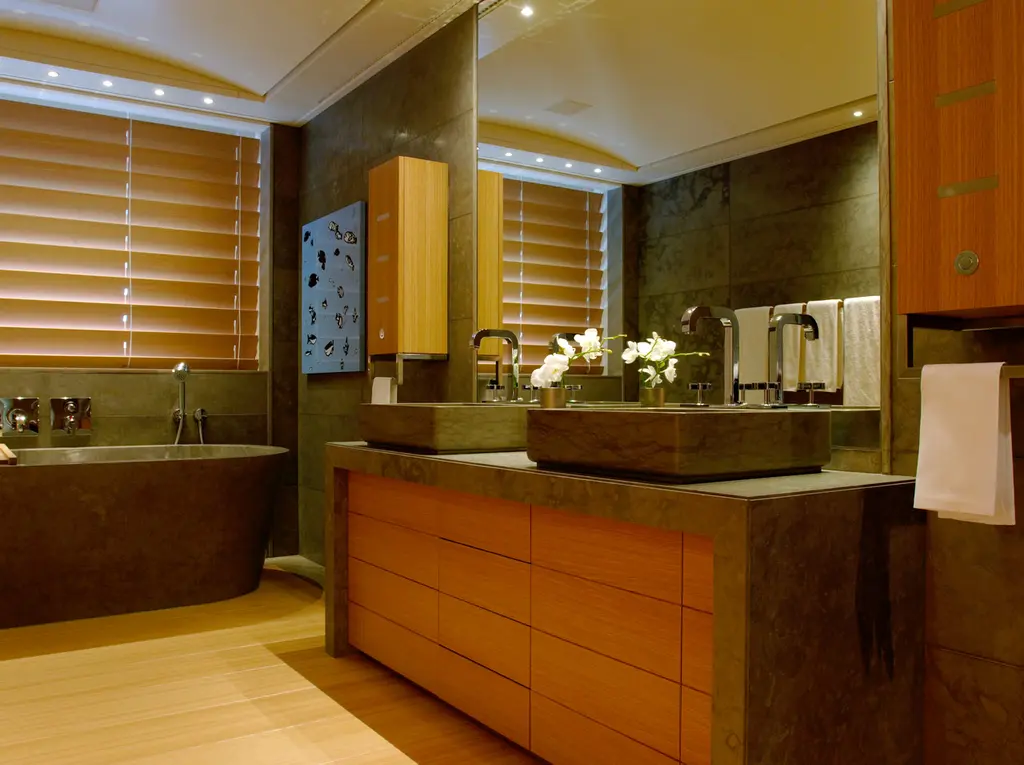 A bathroom with a stone tub, a stone counter with basins and timber cabinets