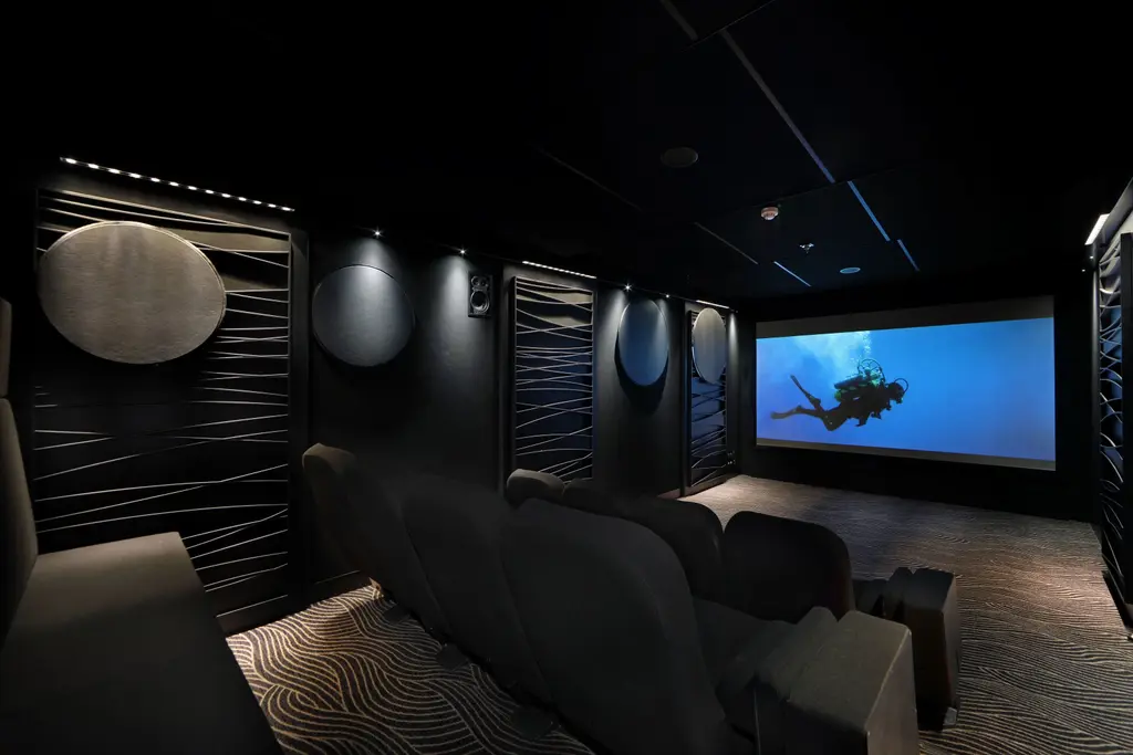 Dark cinema room with rows of armchairs facing a large screen showing a diver