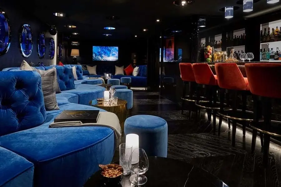 Dark nightclub with blue tufted sofas, a bar with red stools and round illuminated panels on the wall