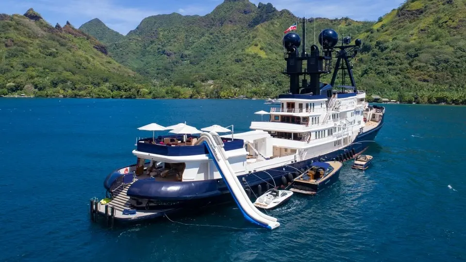 Arctic at anchor with an inflatable water slide running down her side and tenders and toys in the water around her