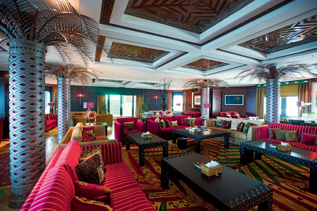 Large salon with palm-shaped columns, red striped sofas and low dark tables