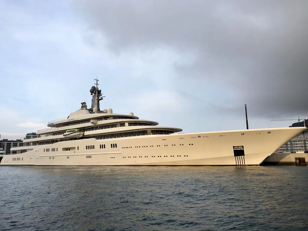 Eclipse moored alongside a quay under grey cloud, seen from the bow quarter