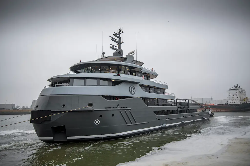 The bow of Ragnar from the waterline in an industrial harbour, showing the blunt icebreaking stem and a dark grey superstructure