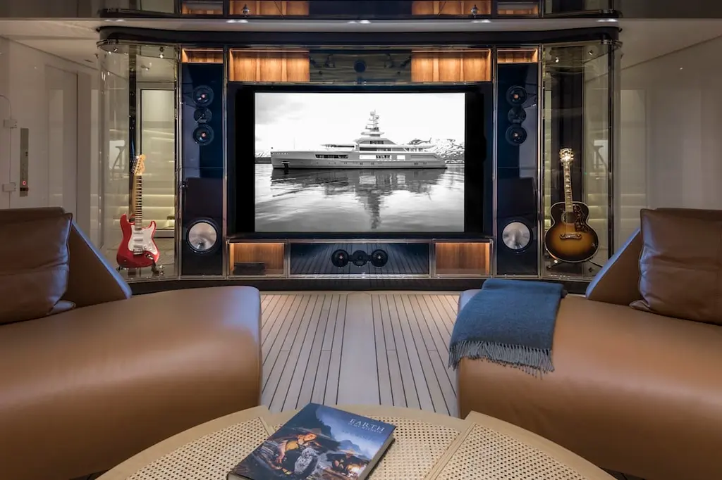 A media lounge with leather armchairs facing a large screen flanked by speakers and guitars
