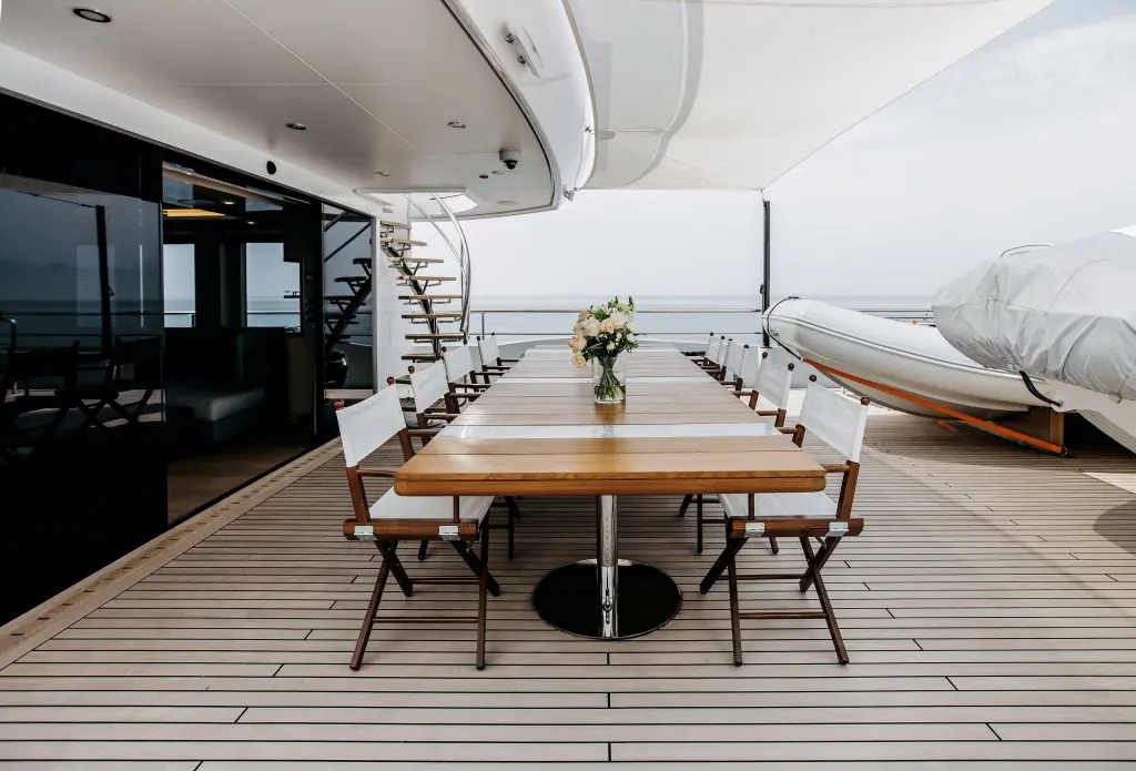 Teak aft deck with a long dining table beside a covered tender in its cradle