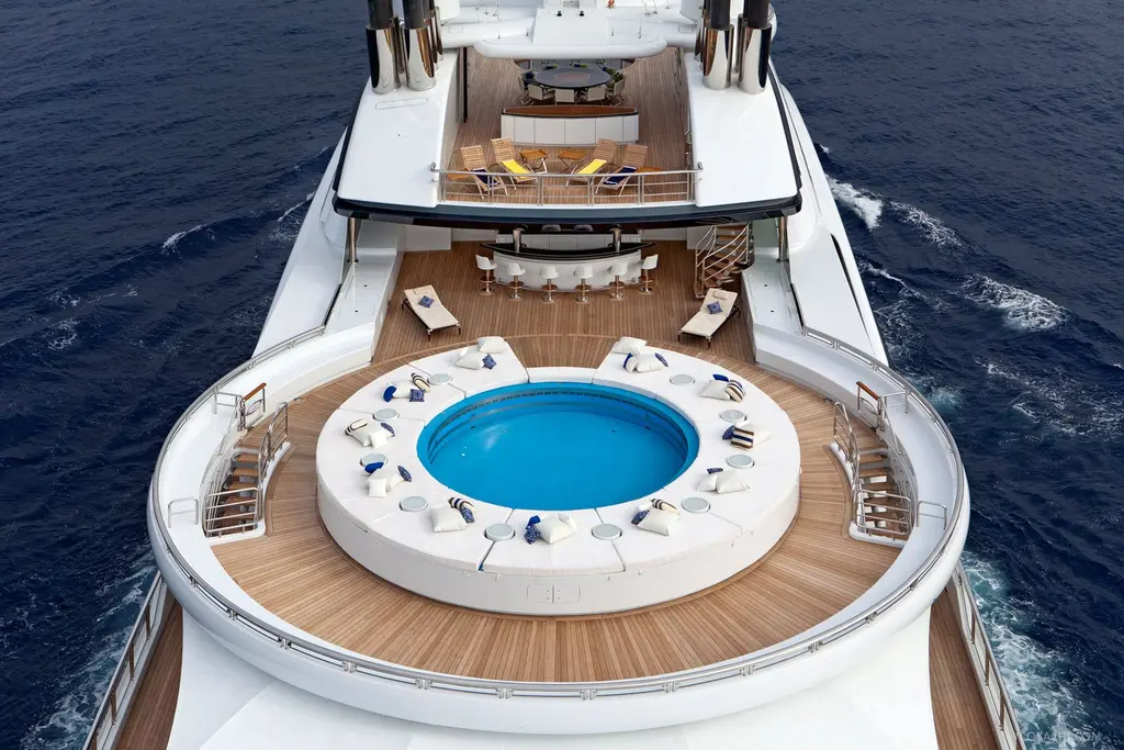 Round pool surrounded by sunloungers on an aft deck of Serene, with a bar and dining area beyond