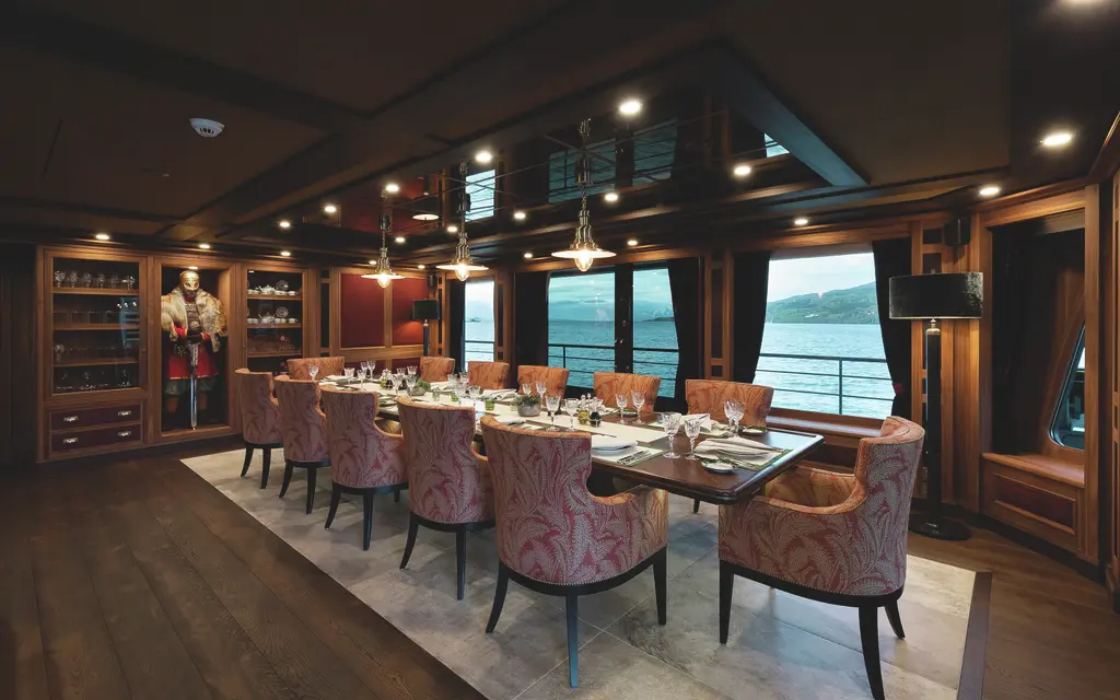 A dining room panelled in dark wood with a long table and patterned chairs, wine cabinets and a full-size figure of a Viking warrior in a niche