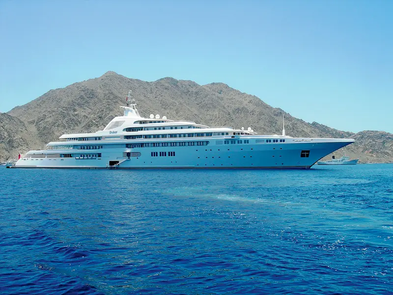 Dubai at anchor in clear blue water in front of a bare rocky mountain