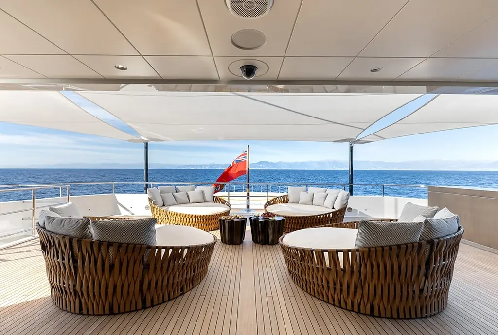 Round woven lounge seating on a covered teak aft deck, with the sea beyond