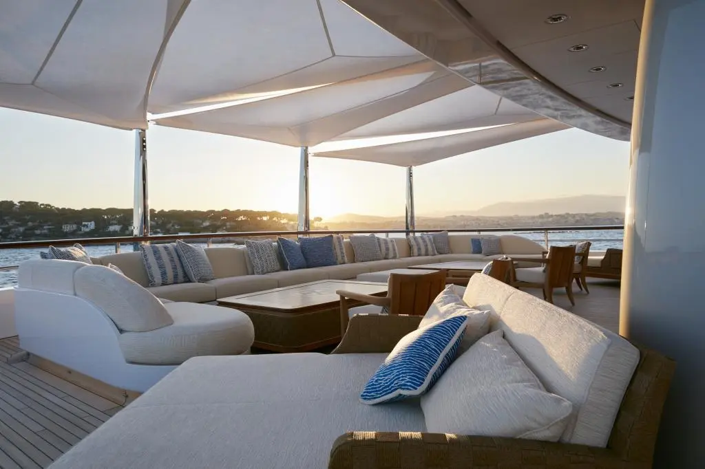 Shaded deck lounge with white sofas under sail-cloth awnings at sunset