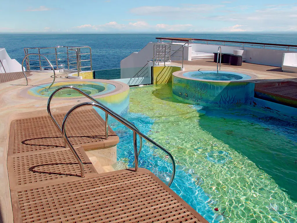 Tiled swimming pool and two round spa pools on deck, sea in the background