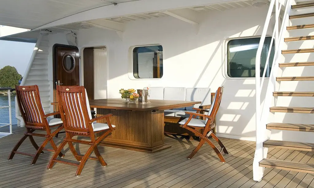 Teak aft deck with a wooden dining table and chairs and a ladder to the deck above, before the 2021 refit