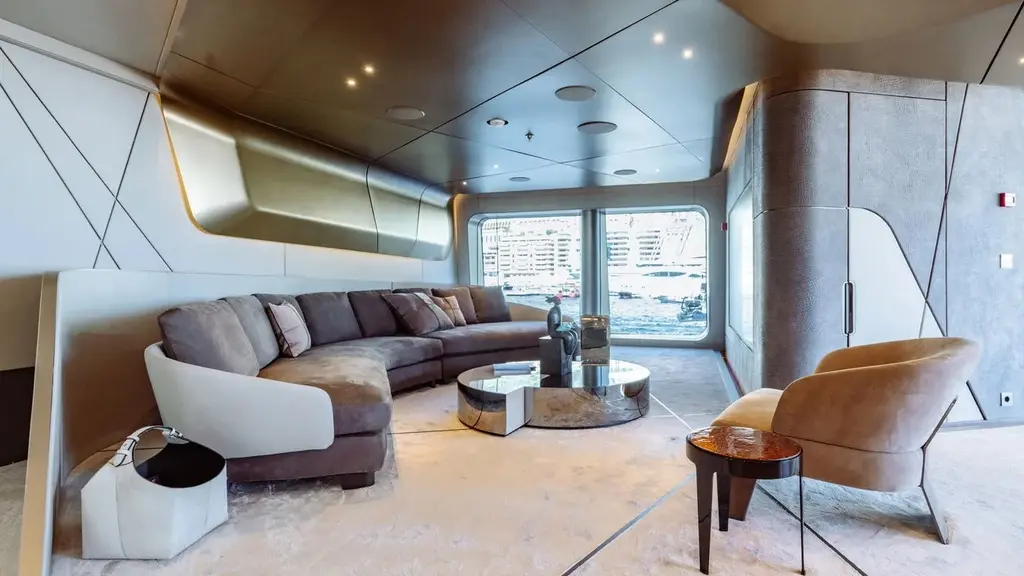 Lounge with a curved grey sofa, a mirrored coffee table and a window to the harbour