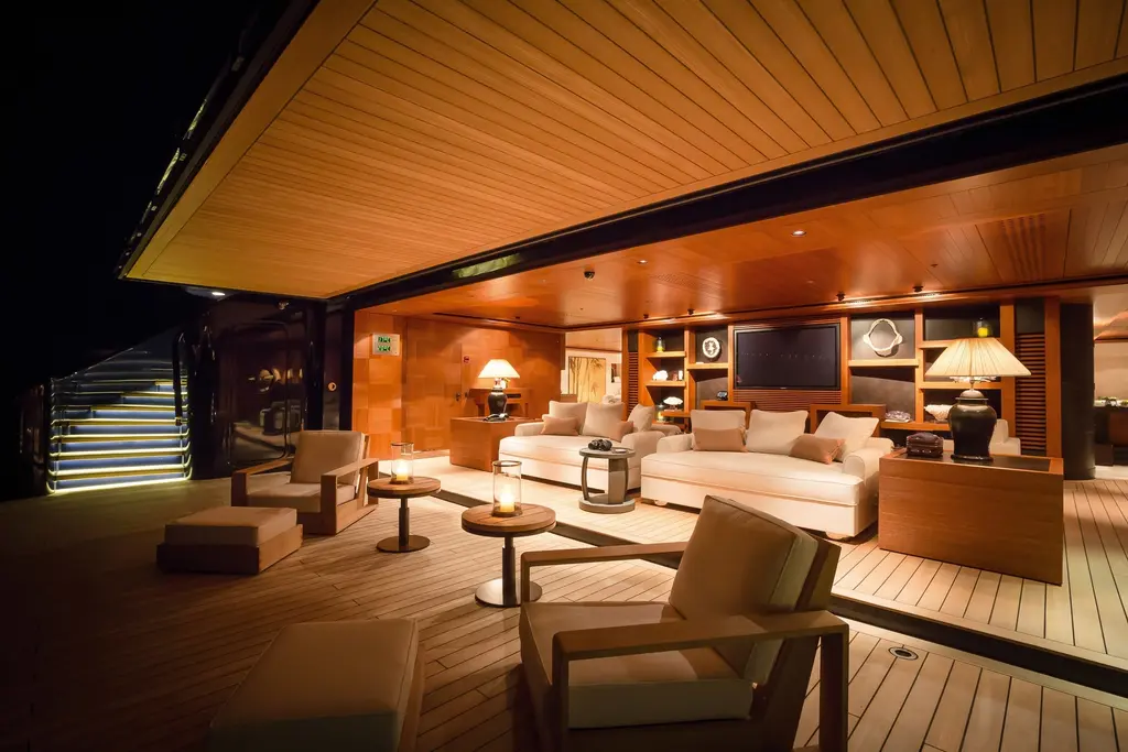 Open-air lounge with wood panelling, sofas and armchairs, lit at night