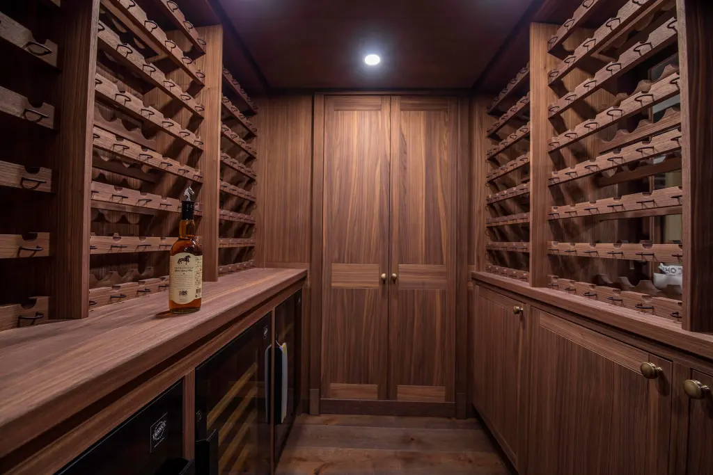 A walnut-panelled wine cellar with racks on both sides and a whisky bottle on the counter