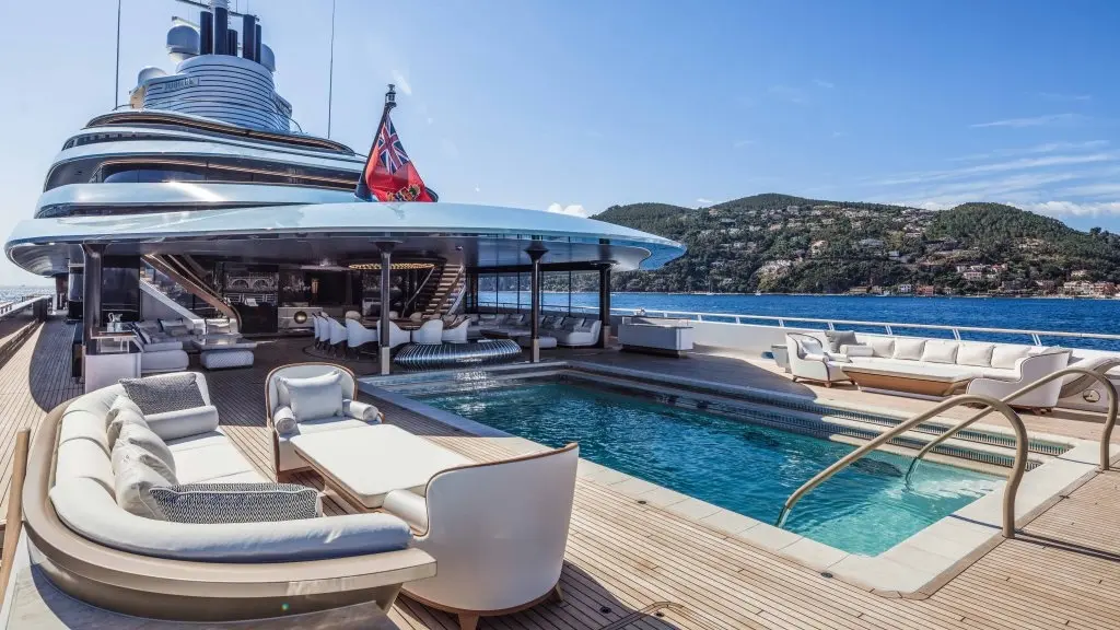 The main deck aft with the swimming pool, outdoor sofas and the hillside of a bay behind