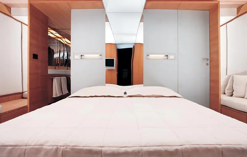 Cabin with a double bed between wood-panelled walls and white cupboards