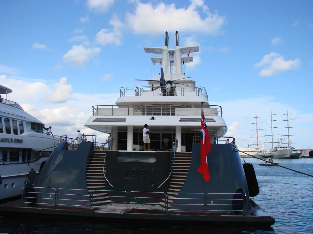 Ice moored stern-to at a quay with her stern stairs down and a red ensign flying, a three-masted ship in the background