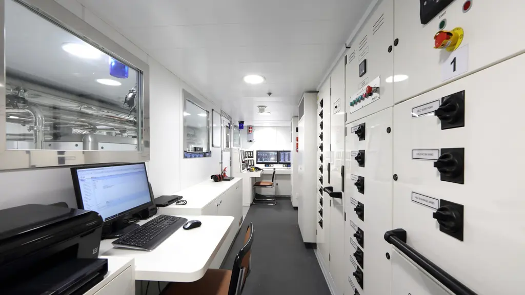 Engine control room with a computer workstation, a window into the engine room and switchboard panels