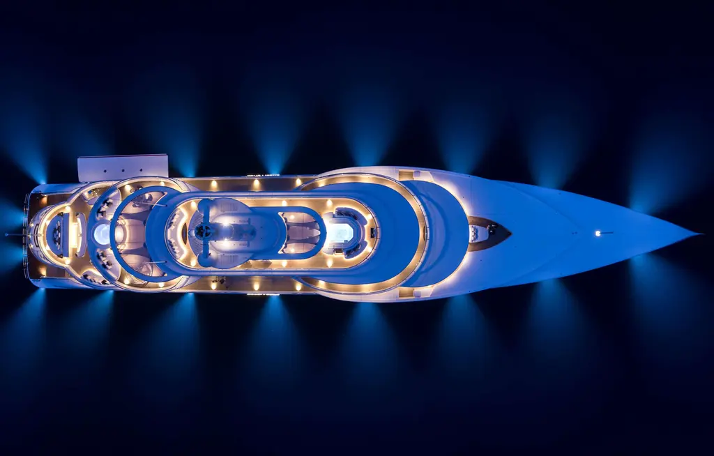 Excellence seen from directly above at night, decks lit and underwater lights glowing blue around the hull