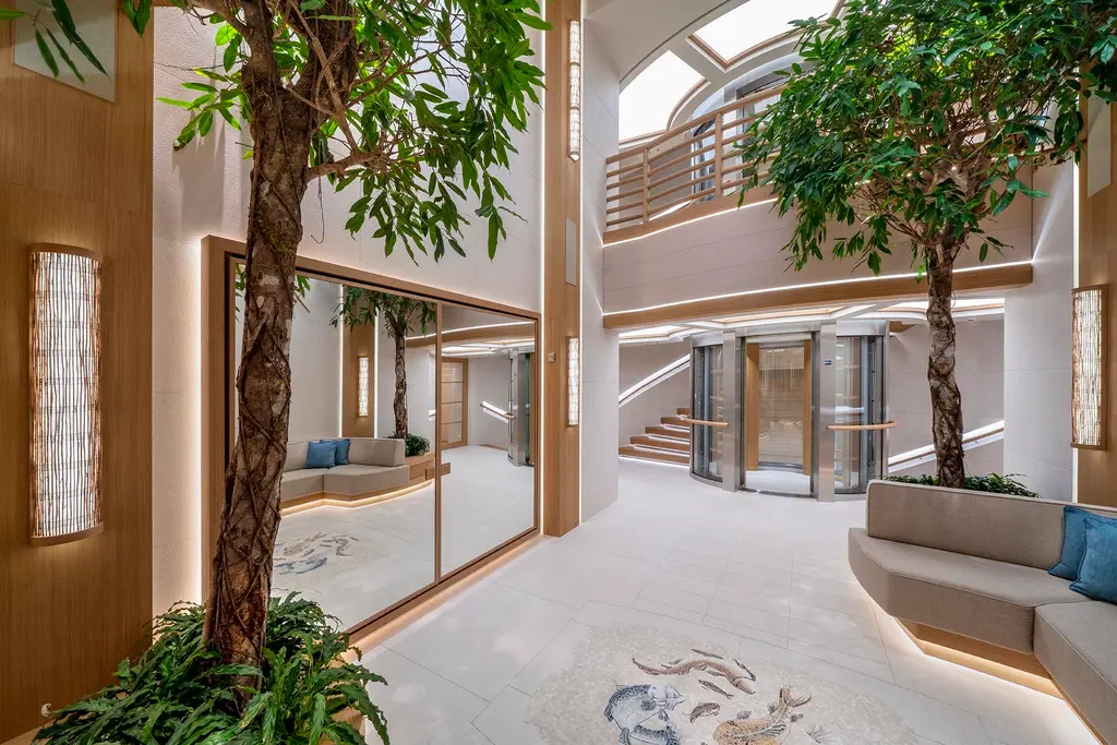 Double-height lobby with indoor trees, a skylight and glass lift