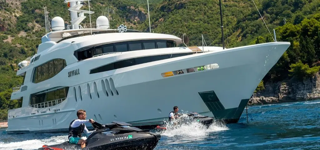 Two jet skis running past Skyfall's bow close to a rocky shore