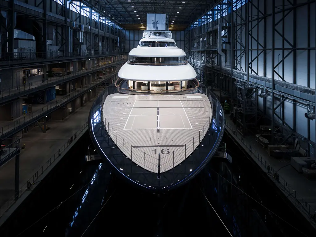 Breakthrough inside the build hall seen head-on, a court marked out on her teak foredeck and four decks of superstructure behind