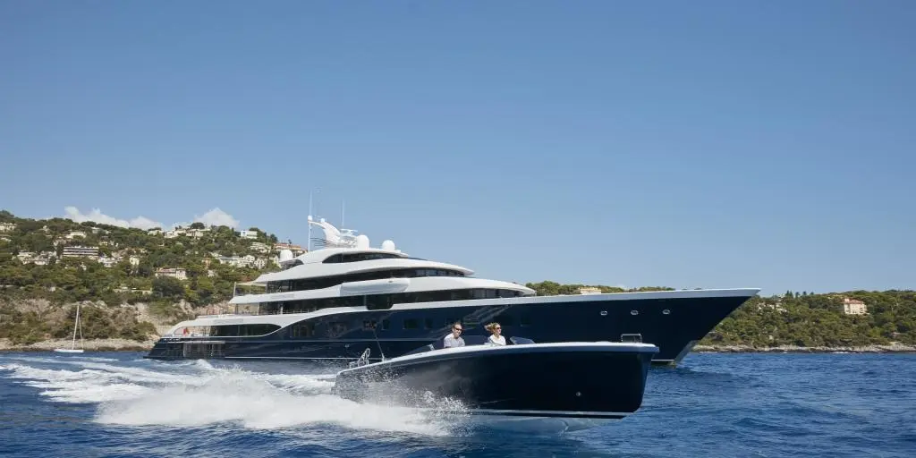 Symphony underway near a green coastline with her navy-blue tender speeding past