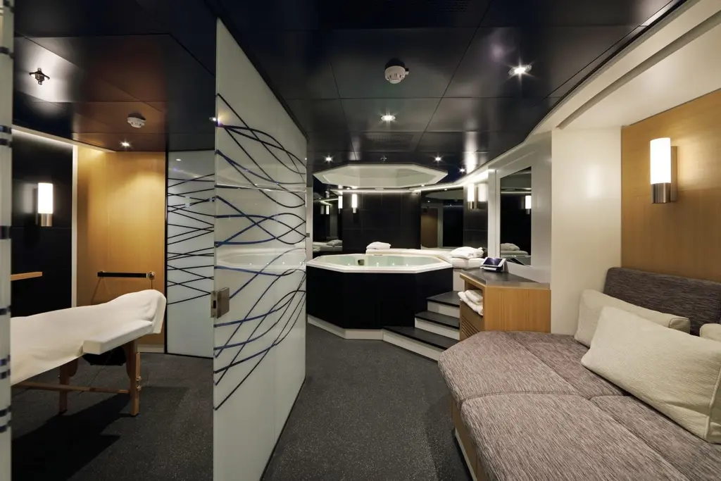 Spa with a hot tub, a massage table and a lounger under a dark ceiling