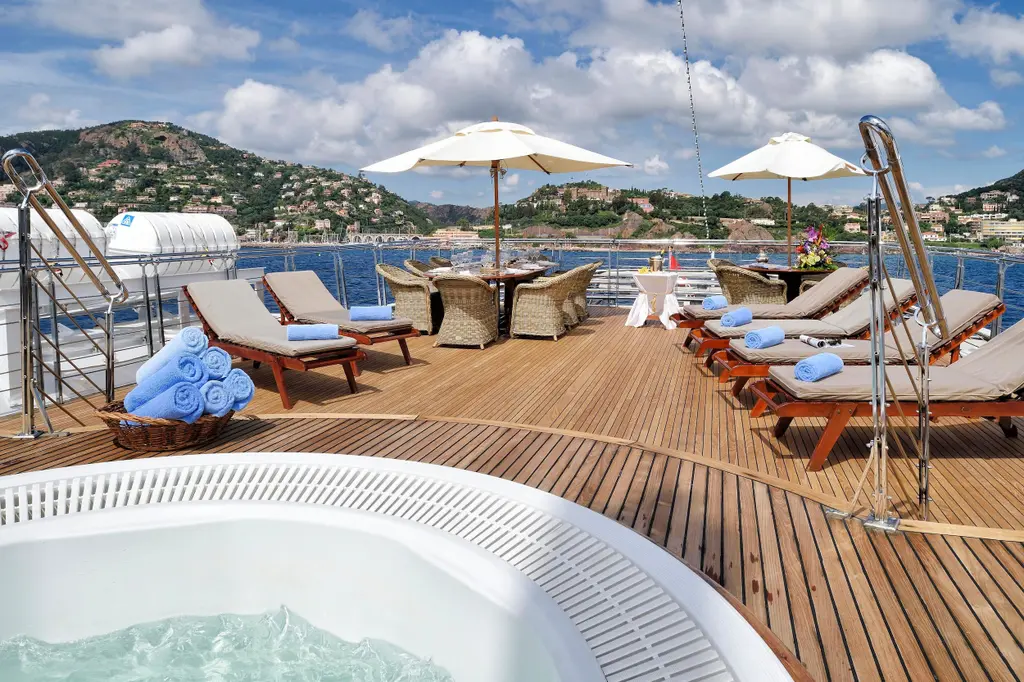 Teak deck with a Jacuzzi in the foreground, sun loungers and parasols behind