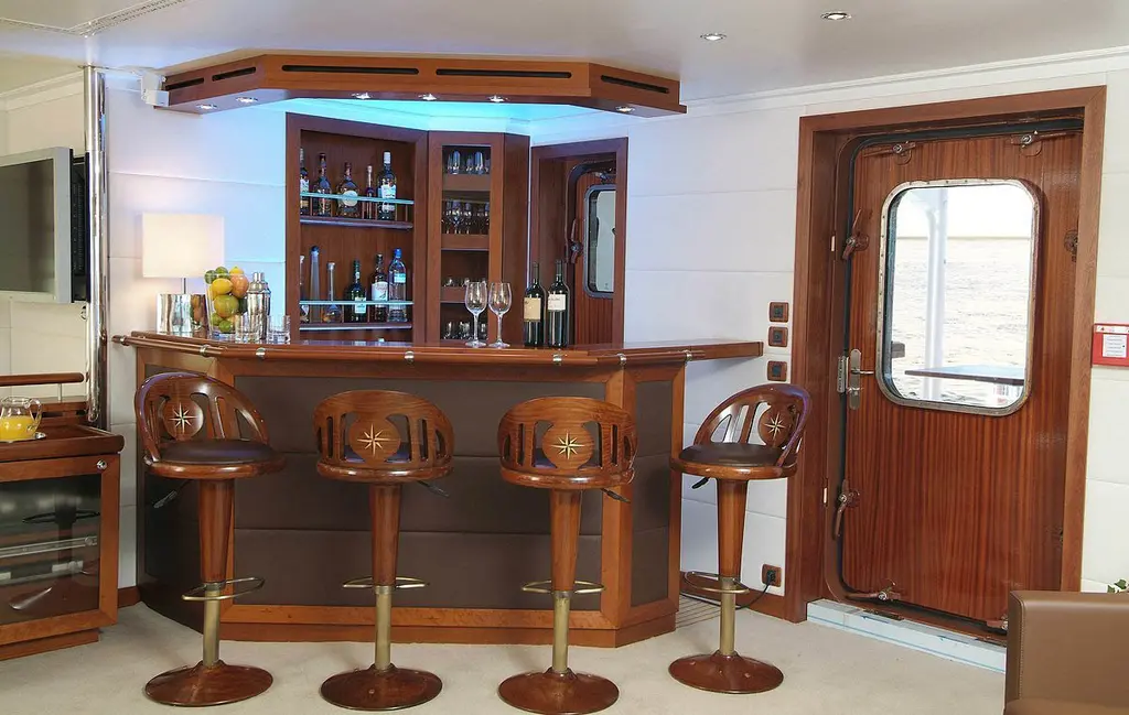 Wooden bar with four stools and a ship's door with a porthole window, before the 2021 refit