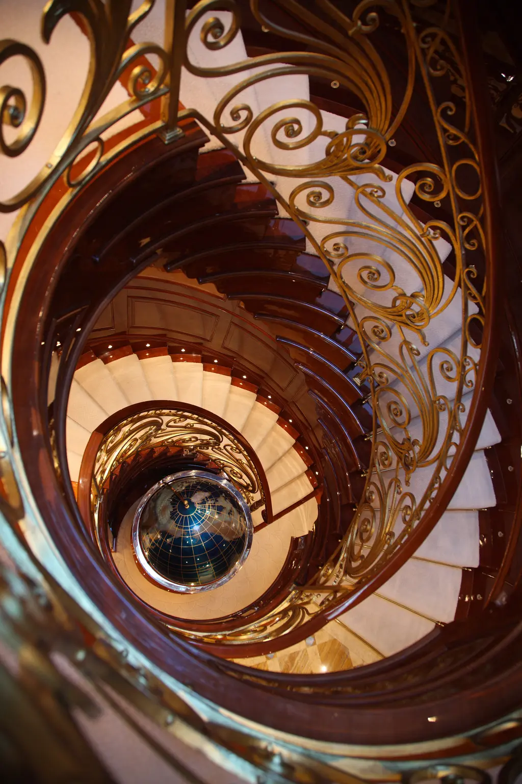 Spiral staircase with gilded scroll balustrades seen from above, a globe at the bottom