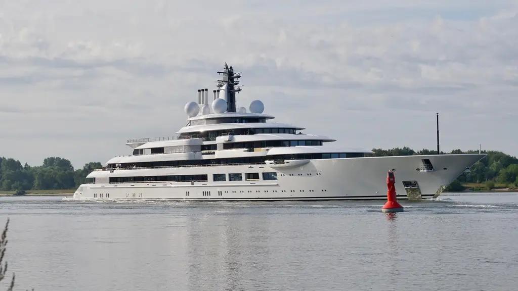 Scheherazade underway on a river under an overcast sky, seen from the starboard side with a red buoy in the foreground and radar domes above the upper deck