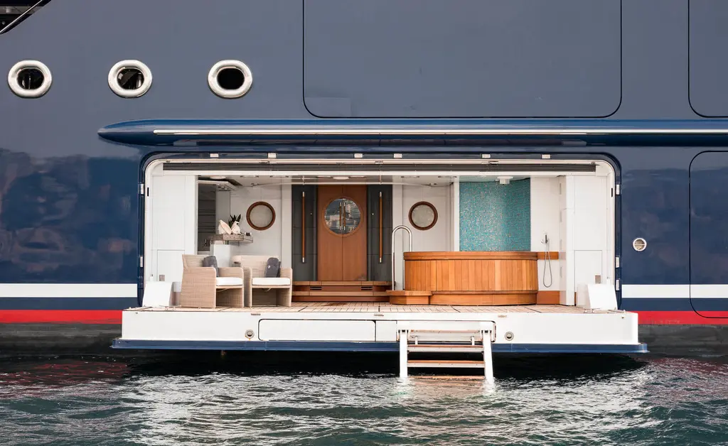 A shell door folded open in the navy hull just above the water, showing a lounge with steps down to the sea