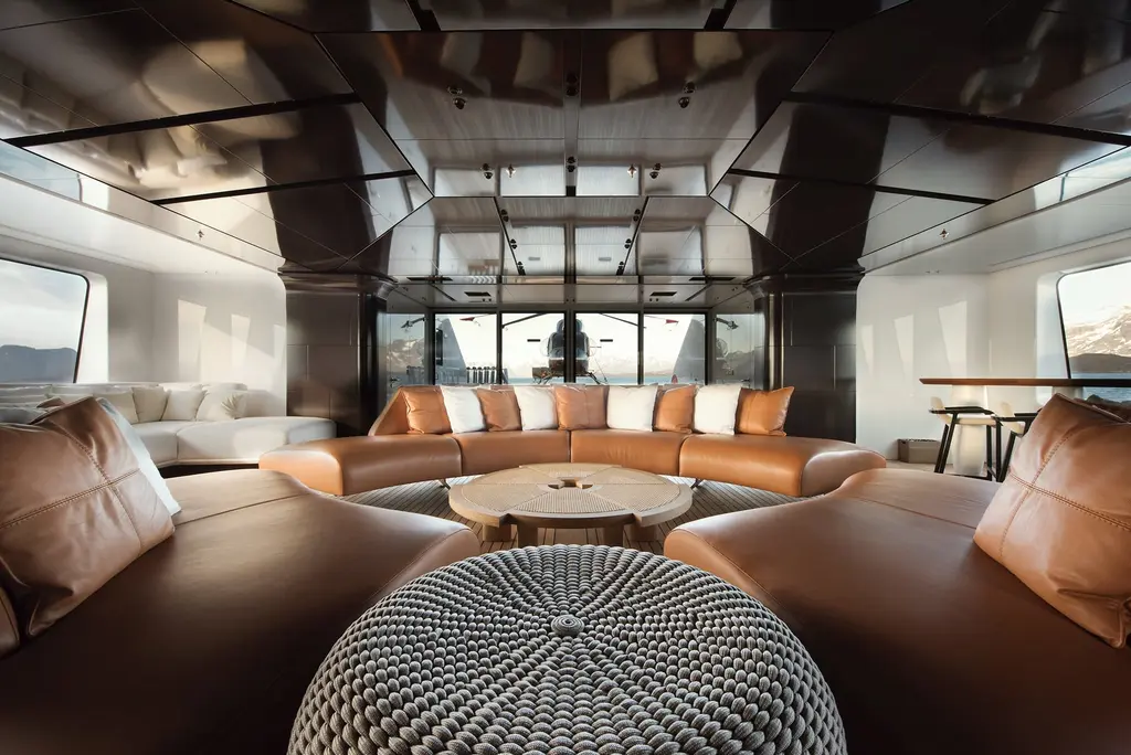 A lounge with a curved leather sofa around a round table and a woven pouf, under a glossy ceiling