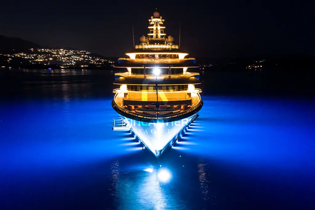 Ocean Victory at night seen head-on from the bow, with blue underwater lights and the superstructure lit