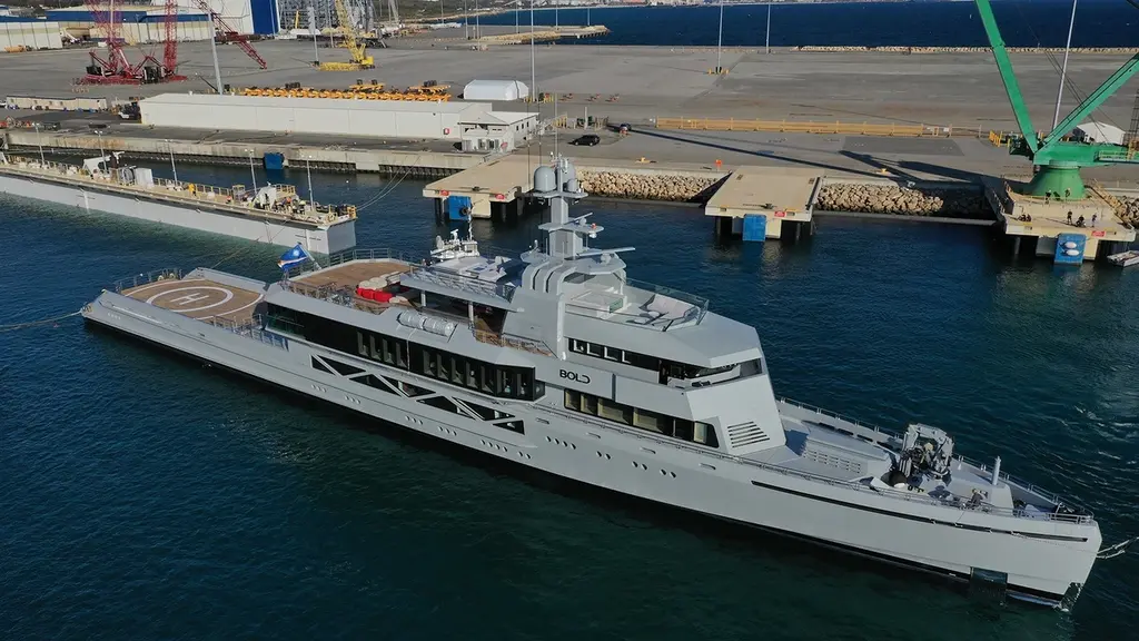 Bold seen from the starboard side and above in a working harbour, with cranes on the quay behind and the helipad on the aft deck